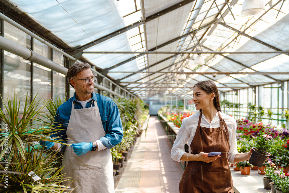 White woman and man wearing aprons standing by plants in greenhouse White woman and man wearing aprons standing by plants in greenhouse