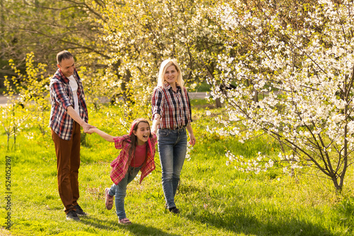 Outdoor portrait of happy young family playing in spring park under blooming tree, lovely couple with little child having fun in sunny garden