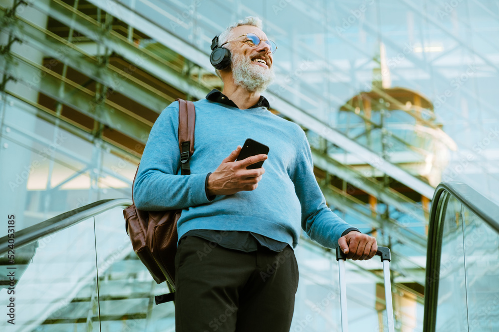 Mature man in headphones using mobile phone while going up on escalator Mature man in headphones using mobile phone while going up on escalator