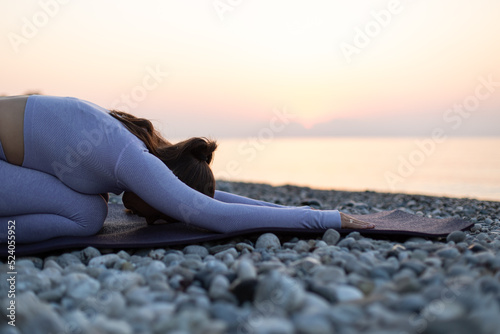 Young woman practice yoga and meditation near the sea at sunrise, healthy lifestyle concept, child pose