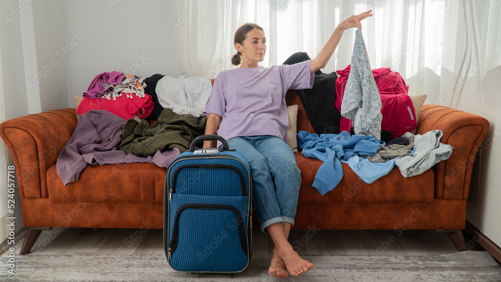 Obraz premium A woman packs a suitcase, decides what to take on a trip, a lot of clothes