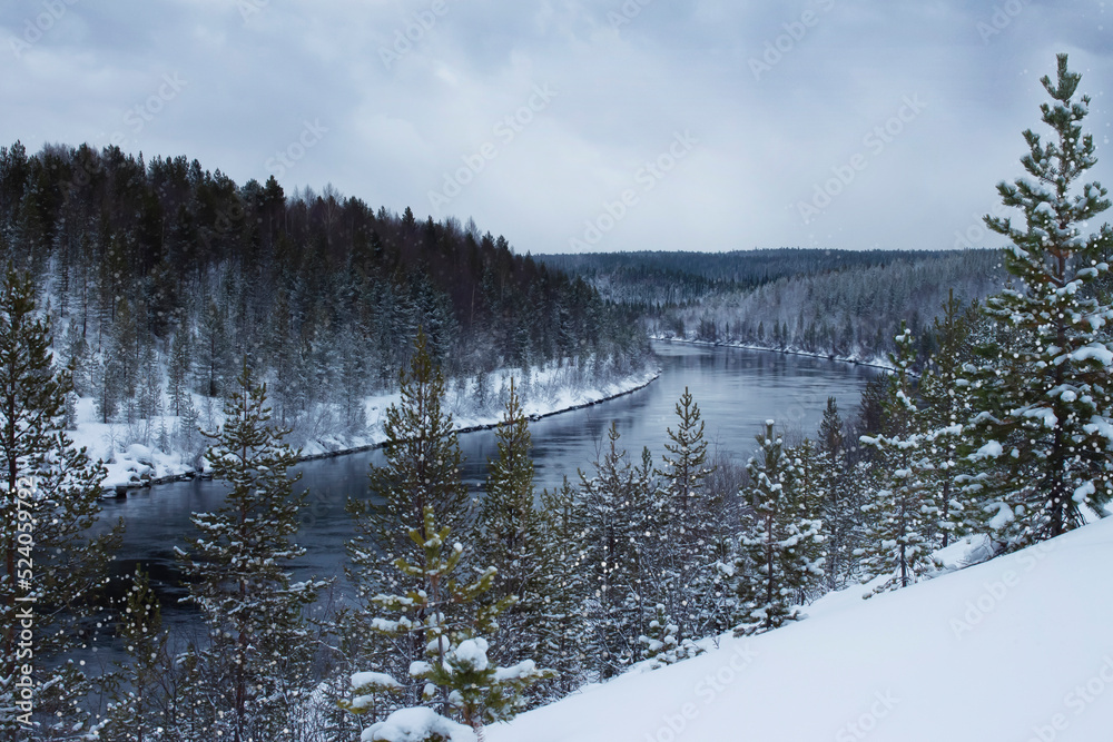 Wonderful winter landscape with snow-covered coniferous forest and river. A place for hiking and traveling. Stunning nature background. Winter river in snow forest. Christmas winter background