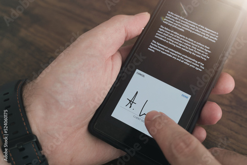 close-up view of electronic signature with finger on smartphone touchscreen against wooden table background photo