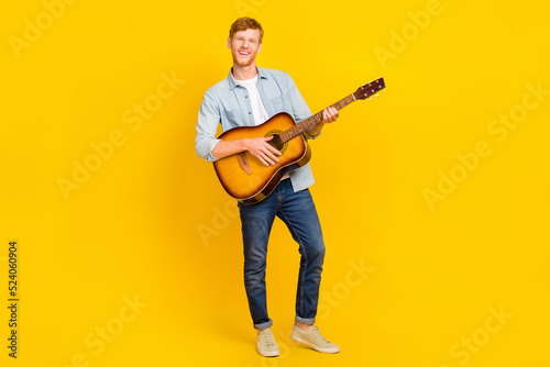 Photo of cute pretty guy dressed denim shirt playing guitar singing smiling isolated yellow color background