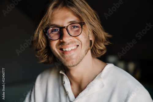 Blonde man in eyeglasses smiling and looking at camera at home