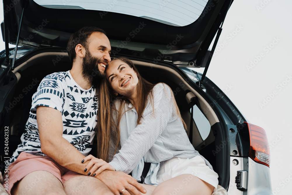 Happy middle-aged couple making stop while on a road trip, caucasian cheerful woman and man sitting in trunk of the SUV car and smiling Happy middle-aged couple making stop while on a road trip, caucasian cheerful woman and man sitting in trunk of the SUV car and smiling