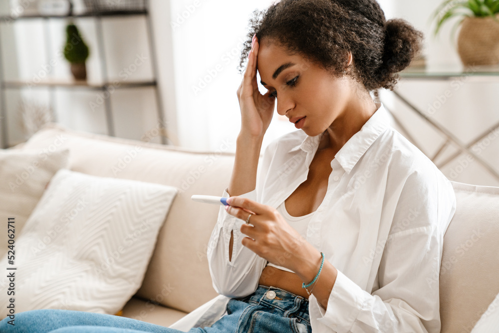 Young black woman being upset while holding pregnancy test at home Young black woman being upset while holding pregnancy test at home