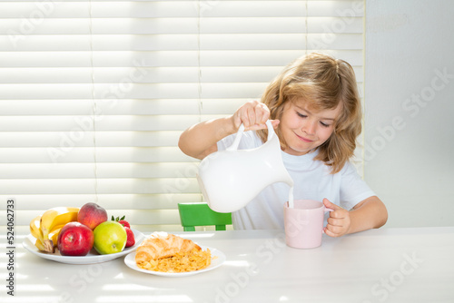 School chil pouring whole cows milk for breakfast. Child in the kitchen at the table eating vegetable and fruits during the dinner lunch. Healthy food, vegetable dish. © Volodymyr