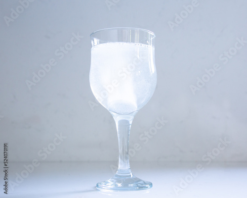 Selective focus closeup of stem glass set on quartz background, with effervescent antacid tablet dissolving in water photo