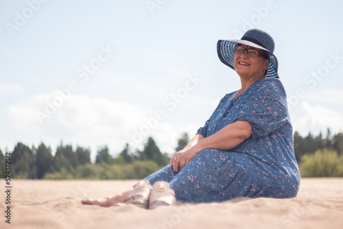 An elderly woman goes sitting on the sandy shore.