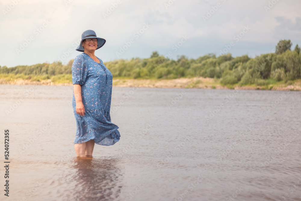 An elderly woman walks along the river bank.
