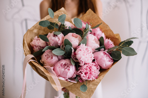 Fototapeta Naklejka Na Ścianę i Meble -  Very nice young woman holding big and beautiful mono bouquet of fresh pink peonies and eucalyptus, cropped photo, bouquet close up