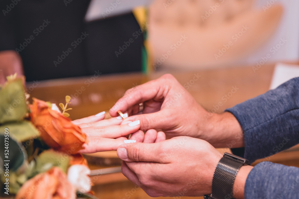 two hands at the moment of exchanging rings between the bride and groom next to a bouquet of flowers