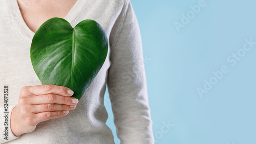 Woman hand holding green leaf on blue background. Environmental and ecology care concept. Green energy, sustainable resources.