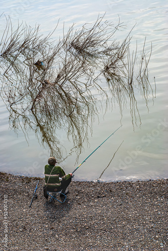 view from above the fisherman catches fish on a fishing rod and sits on a chair, fishing on the river bank in the morning. spring fishing in nature.