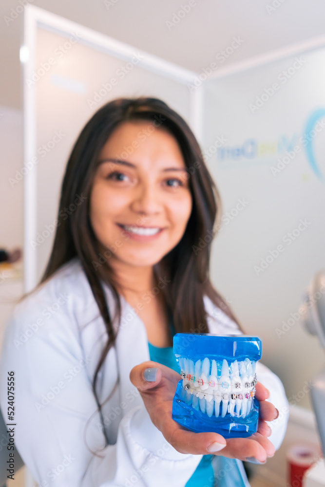 Smiling ethnic dentist demonstrating denture with brackets Smiling ethnic dentist demonstrating denture with brackets