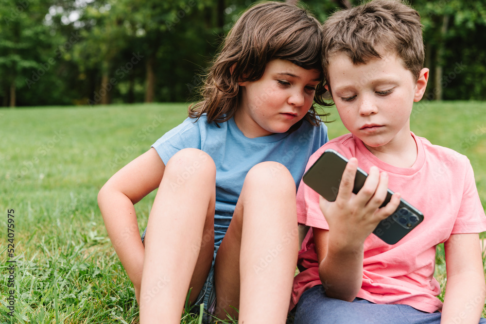 Siblings using smartphone together in park Siblings using smartphone together in park
