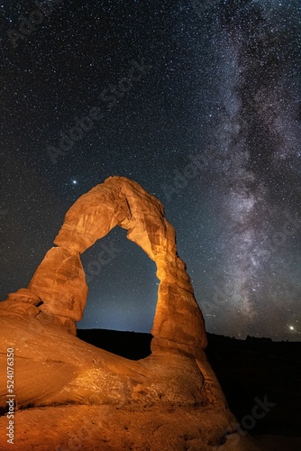 Vertical shot of a stone arch formation under a milky way galaxy sky photo