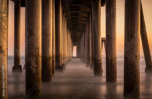 Fotografie, Obraz Landscape of pier with columns on Huntington Beach at golden sunset with steam r