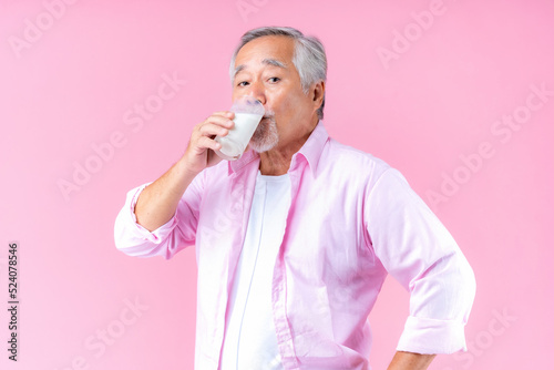 Portrait charming retired asian senior man drinking glasses of milk, happiness elder man wearing shirt pink holding milk in hand enjoying Drink milk for health and bone health pink background.