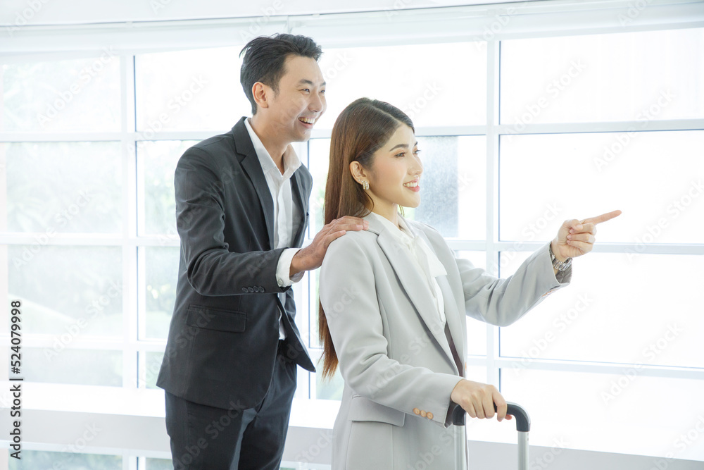 Business couple standing together with baggage and checking time near the window at the departure area at the airport Business couple standing together with baggage and checking time near the window at the departure area at the airport