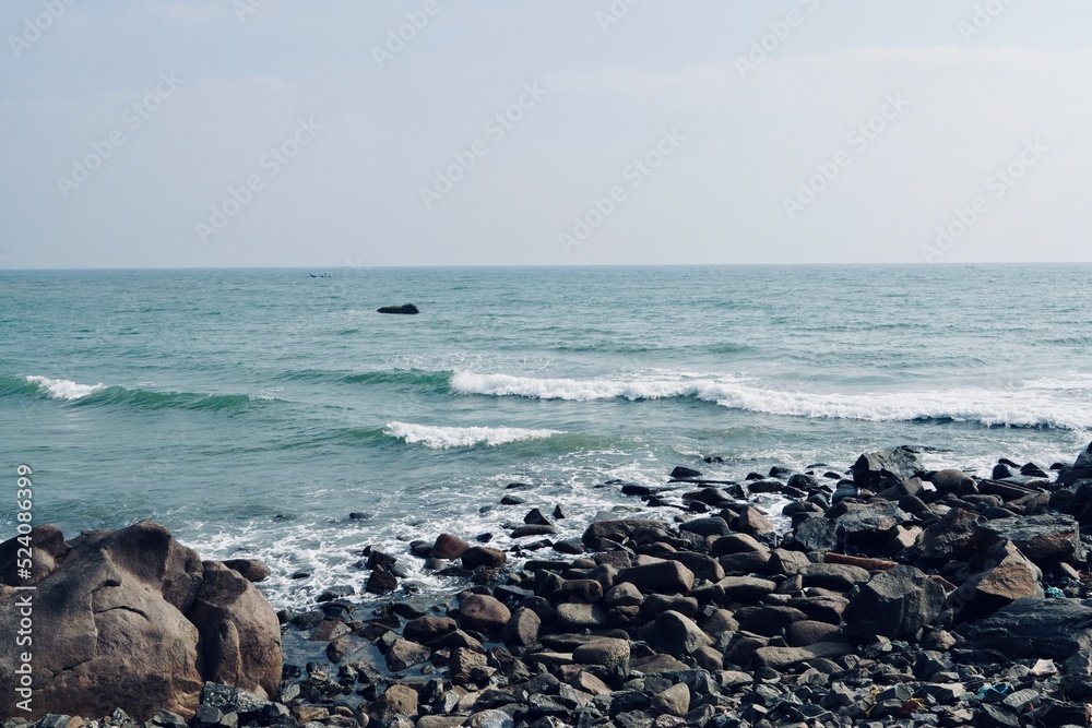 Coastline of Mahabalipuram seashore with constantly hitting sea waves on the rocky stones. Scenic view of seascape with rocks and motion waves in the shore.