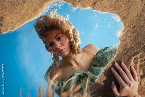 A girl on a sandy beach looks at her reflection in the mirror.