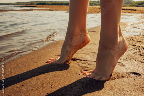 Women's legs stand on a sandy beach.