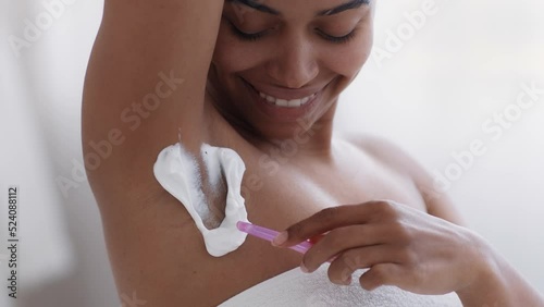 Body hygiene. Close up of young happy african american lady shaving her armpits with pink razor and foam at bathroom