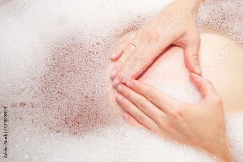Woman hand shaped heart holding on belly pregnant in bathtub. Wedding ring on the finger.