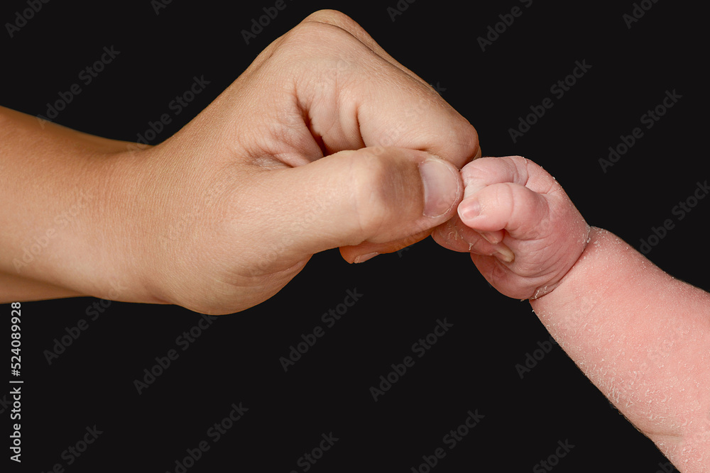 A newborn baby's arm with a clenched fist bumps into its mother's fist