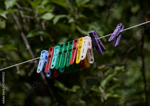 colored plastic clothespins hanging on a rope, photographed against a background of green foliage