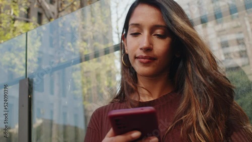 Young businesswoman standing and working with mobile phone in front of glass wall