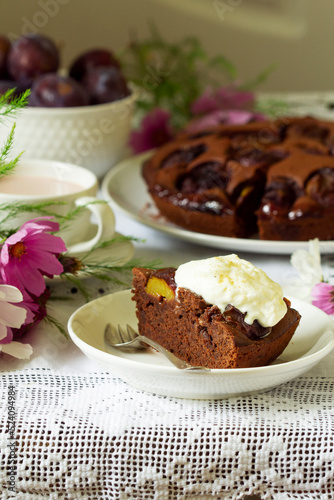Chocolate plum cake with whipped cream, served with cocoa. Rustic style.