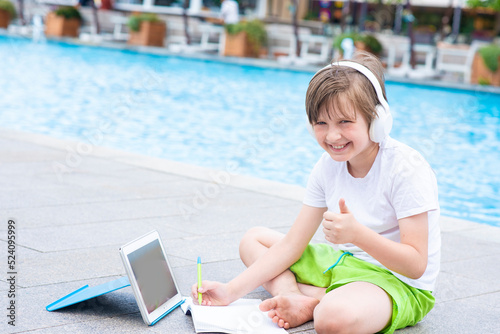little happy boy listen online lesson on vacation at the pool. the child is engaged remotely from anywhere in the world.