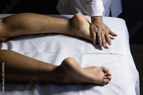 Detalhe das m  os de massagista aplicando massagem terap  utica no p   de um paciente que est   deitado em uma maca com len  ol branco.