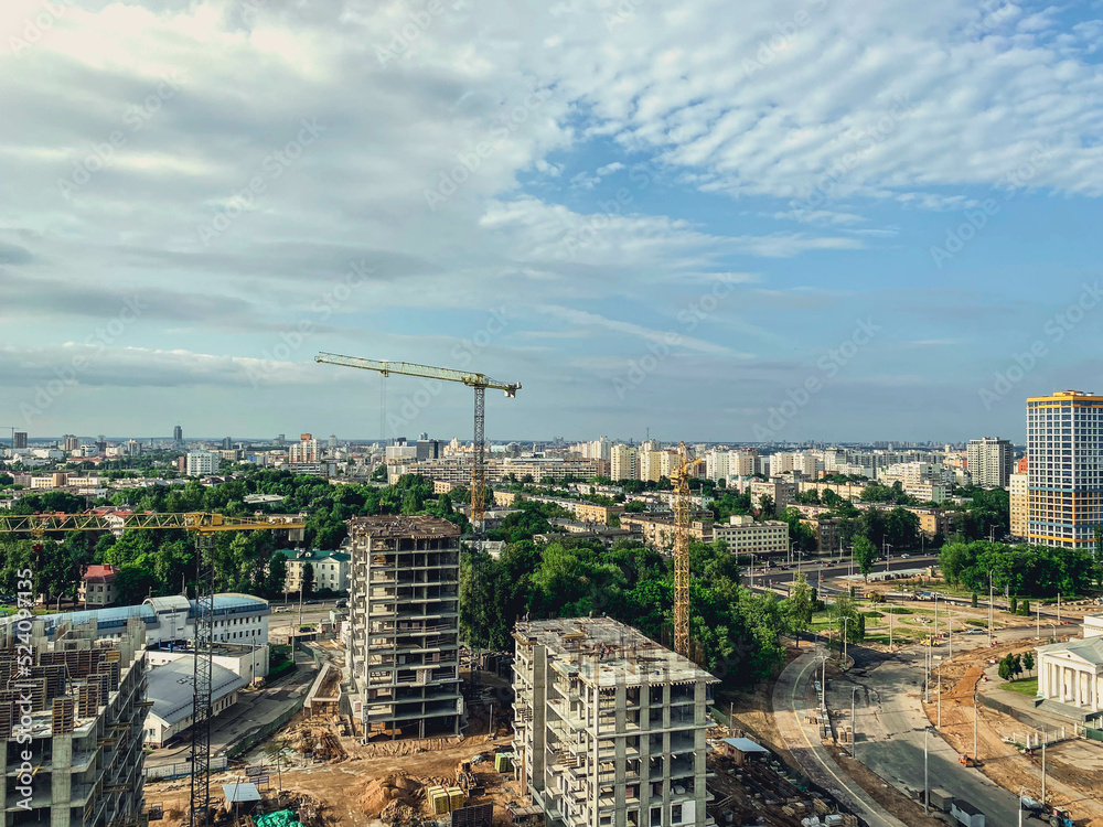construction of multi-storey buildings in the city center. tall houses made of concrete blocks and slabs. a crane erects building material up against a blue, clear sky