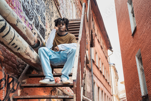 Young handsome stylish black man with natural hair dreadlocks. Afroamerican guy.Stairs,wall painted with graffiti in poor quarter of street art culture city district.African american skateboarder man
