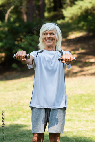 happy senior man in sportswear exercising with dumbbells in green park.