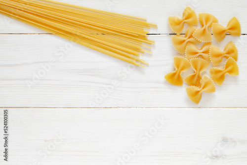 Spaghetti, farfalle, raw pasta, on white wooden board background, top view, space to copy text.