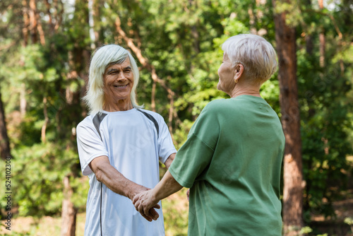 joyful senior couple in sportswear holding hands in green park.