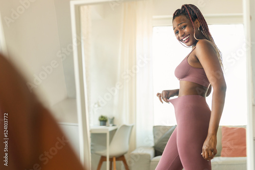 Fit black lady in front of mirror checking training and dieting results, looking at herself and smiling