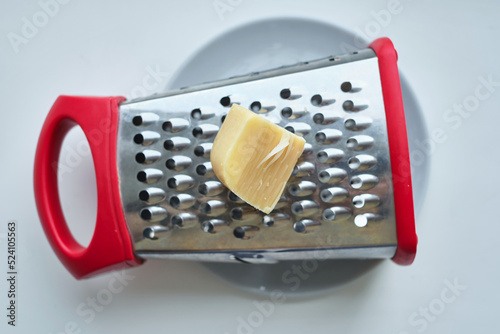 Ggrater and a plate with grated hard tasty cheese on a light background. Dairy. Concept: Italian cuisine, cheese, restaurant and food. Copy space
