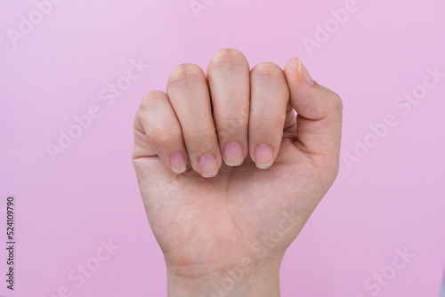 hand of a latin woman showing her nails in a closed hand pose, in the background a pink cardboard, semi arranged nails ready for the realization of a nail painting and decoration.