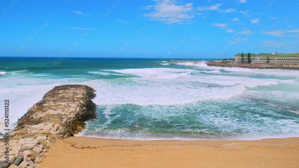 Beautiful azure ocean with sandy beach Baleia on summer sunny day in touristic city Ericeira. Large ocean waves are rolling on sandy beach during tide. Popular beach for travel while vacation. Beautiful azure ocean with sandy beach Baleia on summer sunny day in touristic city Ericeira. Large ocean waves are rolling on sandy beach during tide. Popular beach for travel while vacation.