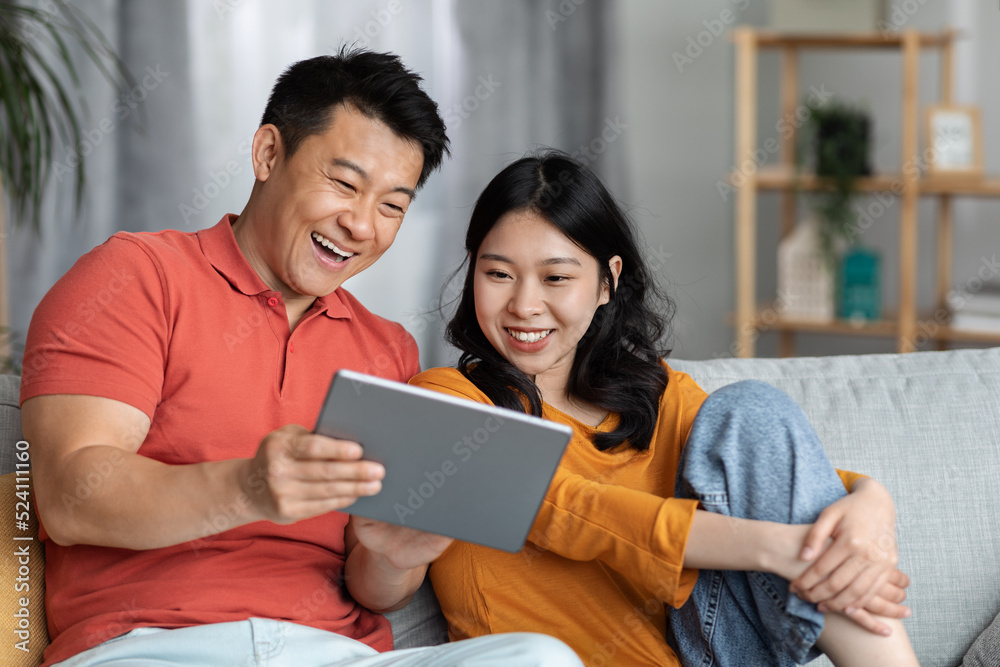 Cheerful asian family sitting on couch at home, using pad Cheerful asian family sitting on couch at home, using pad
