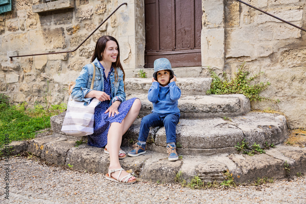 Mother and little handsome baby boy sitting on ancient stone stairs and playing outdoor with straw hat in old town Mother and little handsome baby boy sitting on ancient stone stairs and playing outdoor with straw hat in old town