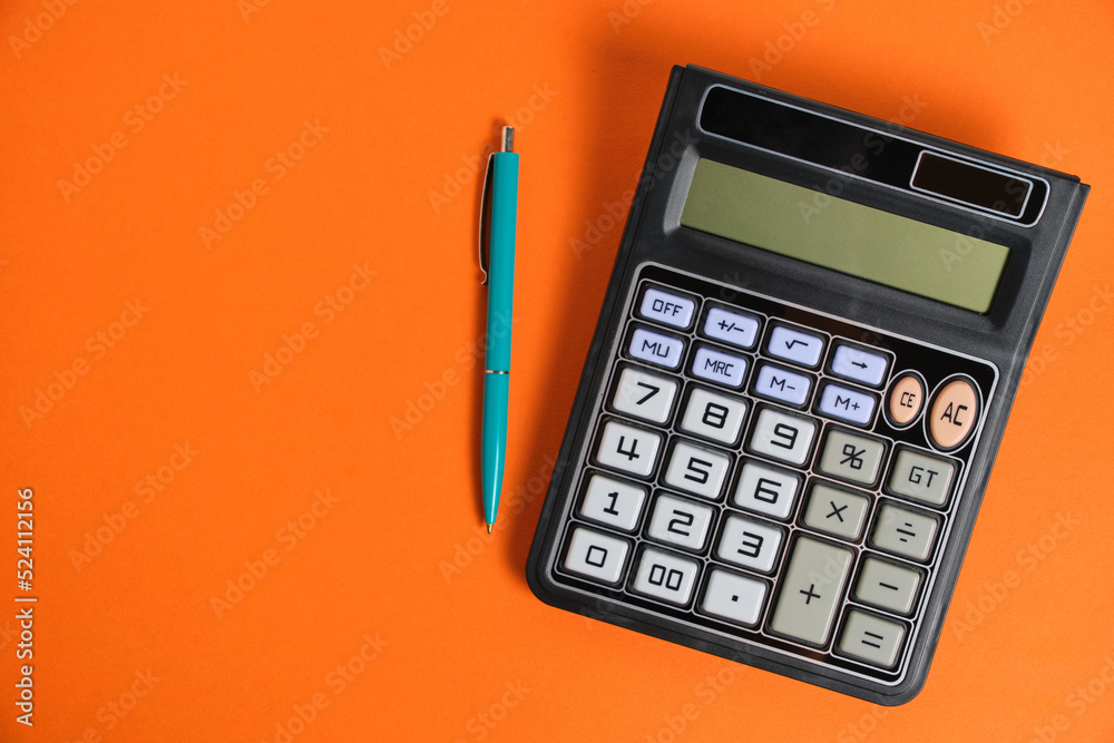Calculator turned off and a ballpoint pen on orange background. Calculator turned off and a ballpoint pen on orange background.