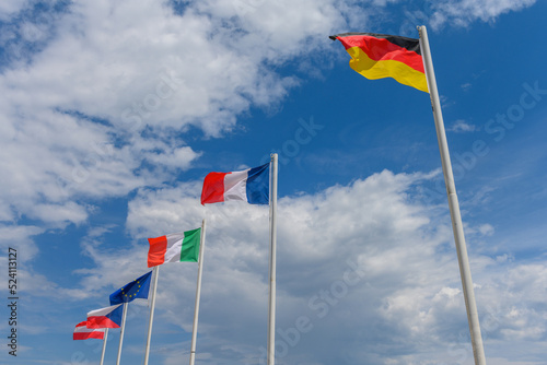 Austrian, French, German, Czech, Italian, and EU flags waving in the wind. It is a beautiful sunny summer day, with blue sky and white clouds in the background.