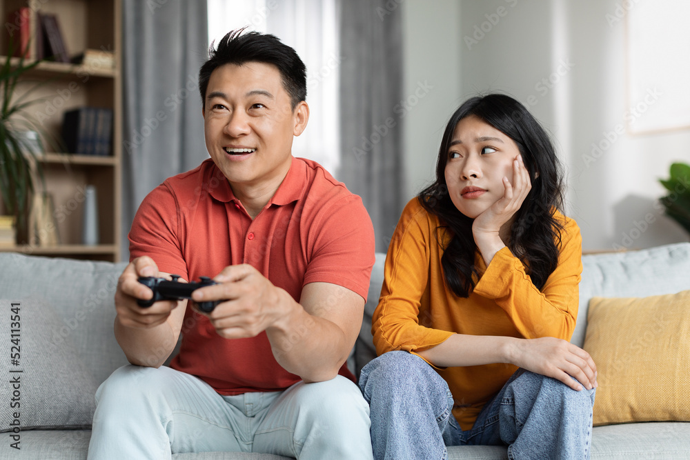 Bored asian woman sitting by her boyfriend playing video games Bored asian woman sitting by her boyfriend playing video games